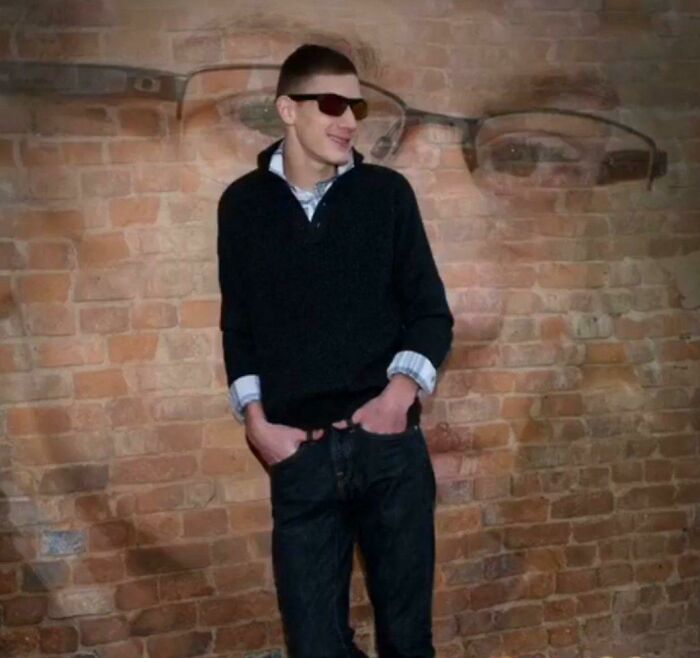 Teen boy wearing sunglasses and a black sweater posing awkwardly against a brick wall in a childhood photo.