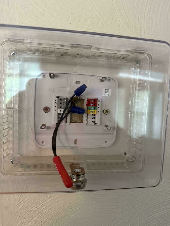 Exposed rental nightmare showing poorly wired thermostat with unsafe electrical connections behind plastic cover.