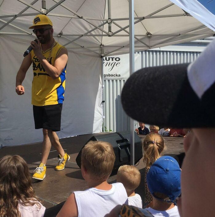 Man in yellow performing on stage under a tent, with children watching, creating a confusing brain moment photo.