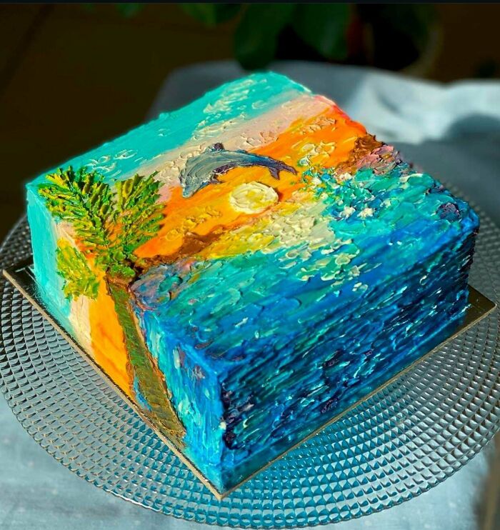 Square cake decorated with masterfully crafted ocean scene featuring a dolphin, palm tree, and vibrant sunset colors.