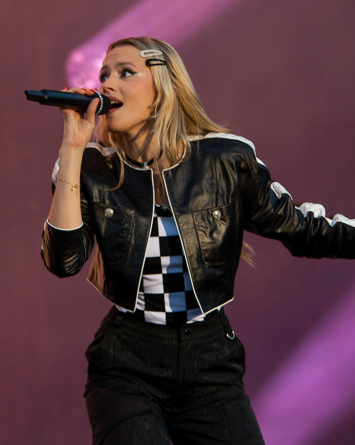 Ang&egrave;le performing live on stage, wearing a black leather jacket and holding a microphone, showcasing her career highlights.