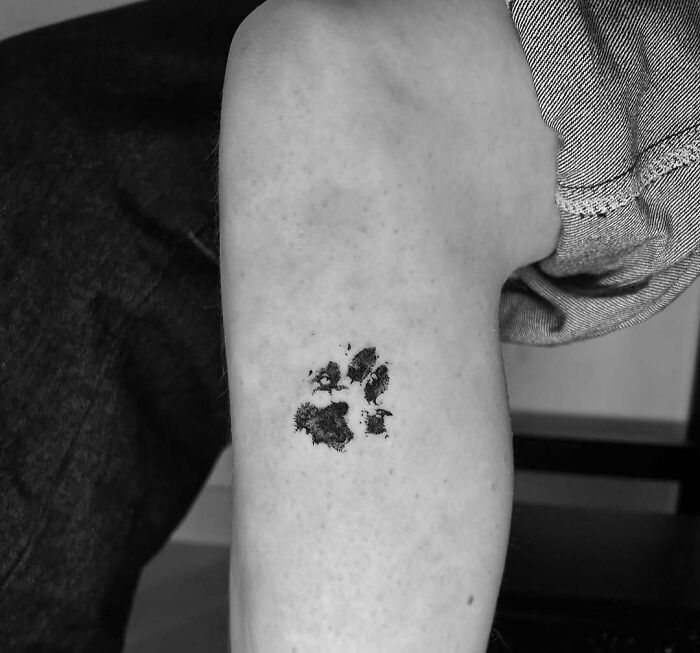 Small black paw print tattoo on inner arm showcasing wholesome tattoos with meaningful ink designs.