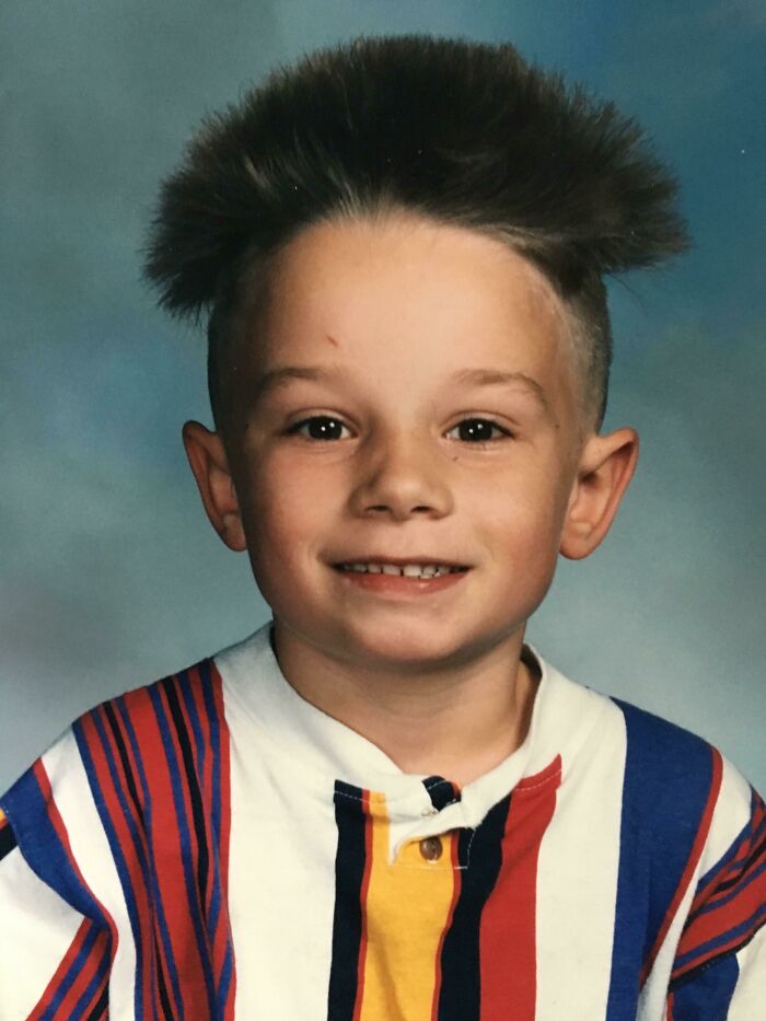 Child with spiky haircut and colorful striped shirt in a hilariously awkward childhood photo.