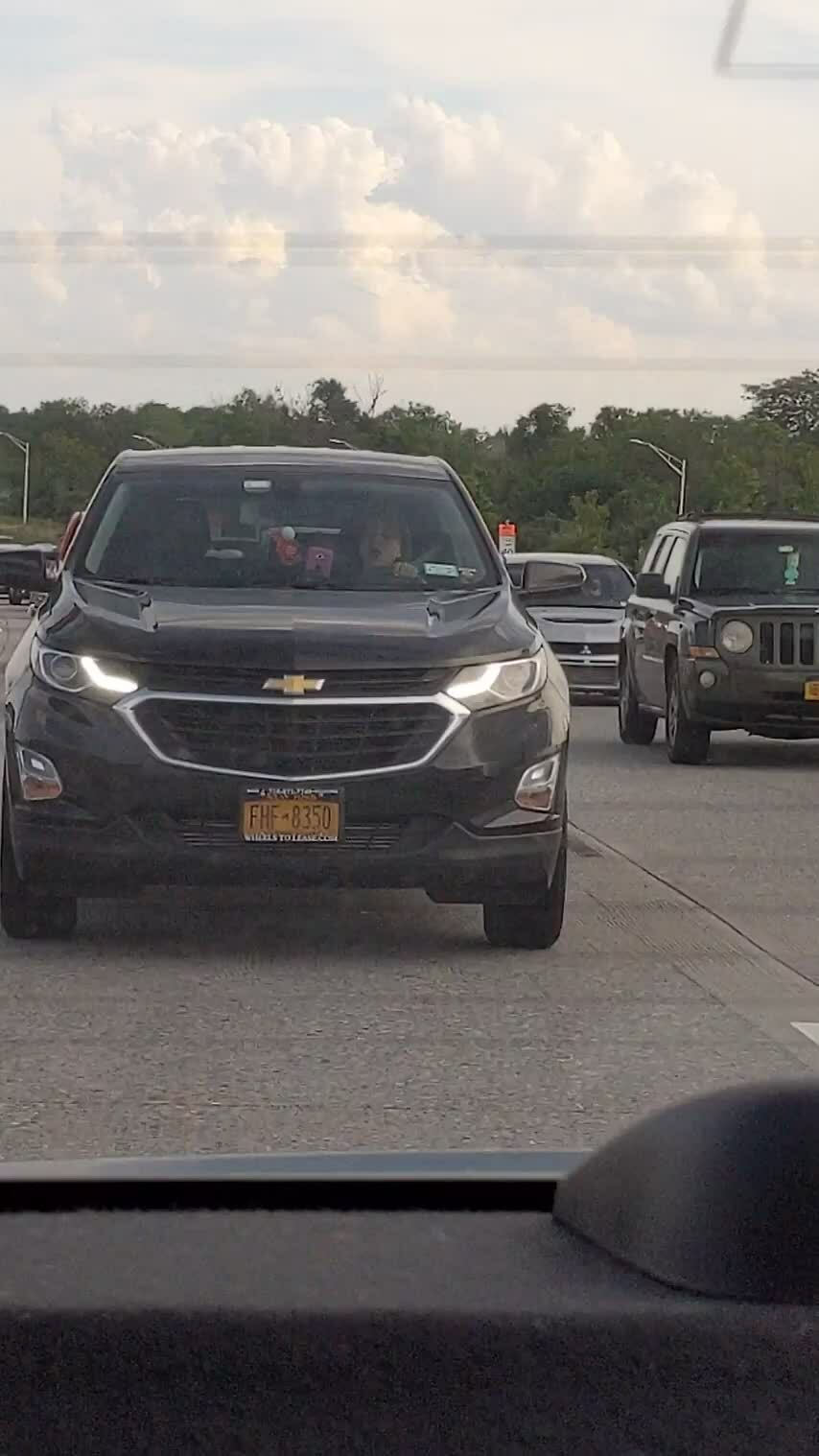 Black Chevrolet car with headlights on driving too close in traffic, a rage-inducing driving moment on a busy road