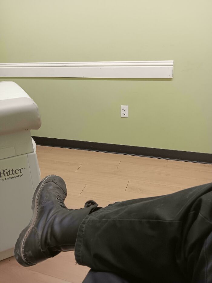 Patient's leg with worn black boot resting beside medical examination table in a calm clinical room setting. Patient's leg with worn black boot resting beside medical examination table in a calm clinical room setting.
