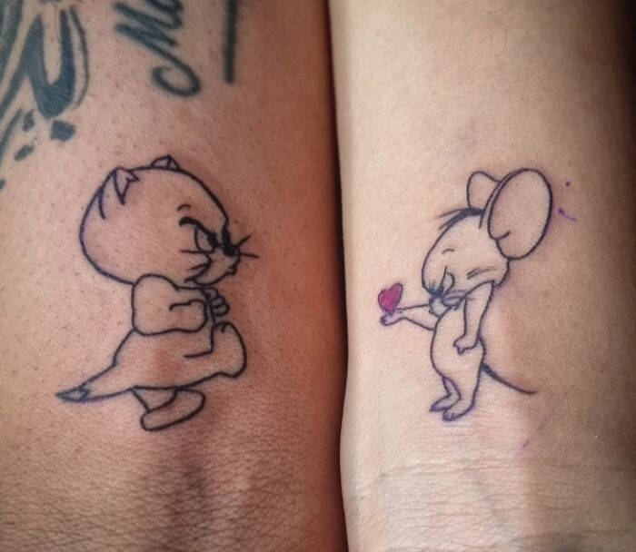 Matching wholesome tattoos of cartoon cat and mouse characters on two different wrists showing meaningful ink art. Matching wholesome tattoos of cartoon cat and mouse characters on two different wrists showing meaningful ink art.
