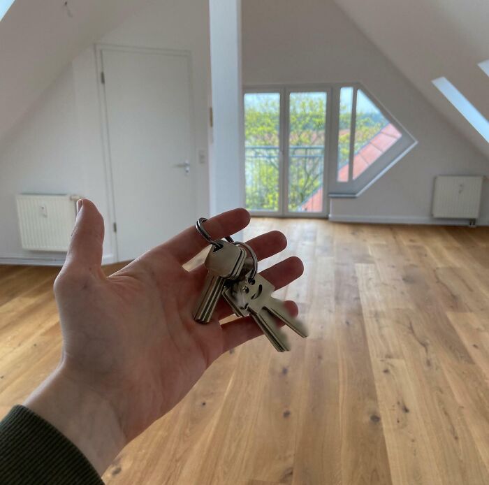 Hand holding keys in an empty room with wooden floor, symbolizing leap of faith and best life decisions.