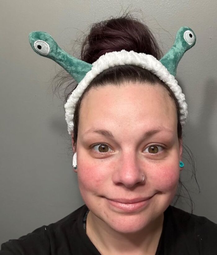 Woman smiling wearing a funny alien headband, a playful idea for white elephant gifts to make stealing fun and lively.