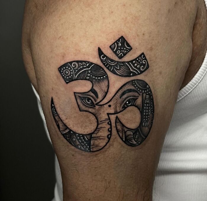 Black ink wholesome tattoo on upper arm featuring a detailed design with an Om symbol and artistic elements.