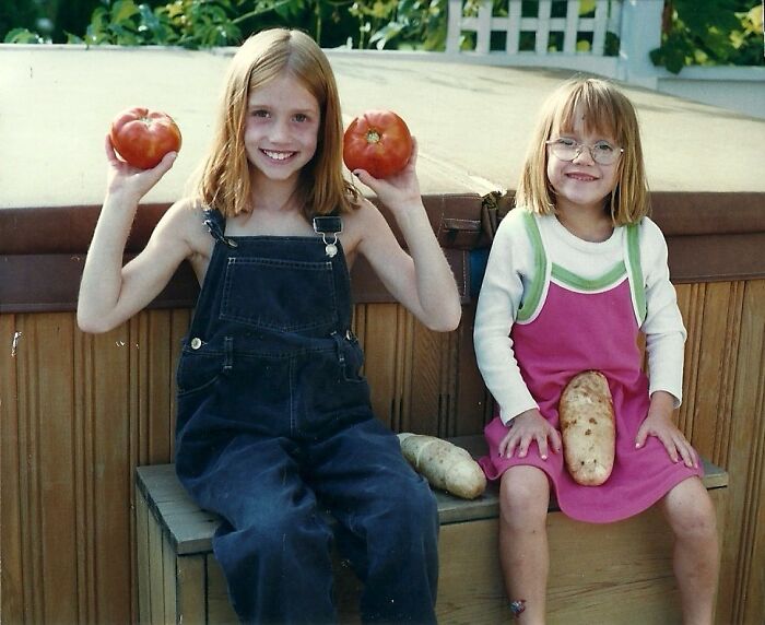 Two children smiling awkwardly holding large vegetables in a backyard, capturing hilariously awkward childhood photos.