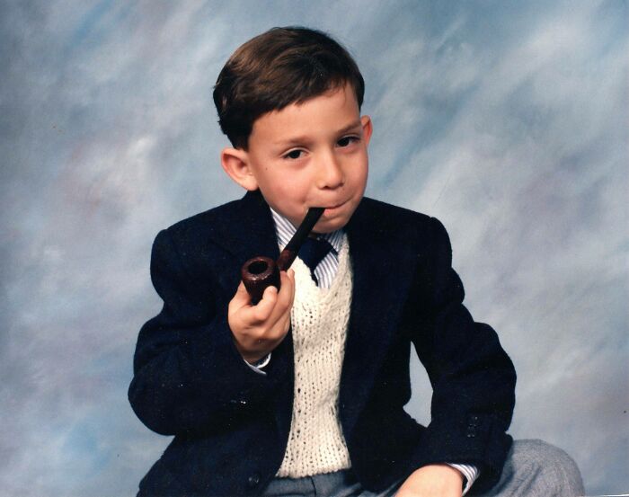 Young boy in a blazer and sweater vest holding a pipe, posing for a hilariously awkward childhood photo.