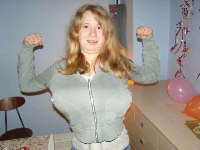 Young girl making funny muscle pose in a casual setting, part of hilariously awkward childhood photos collection.