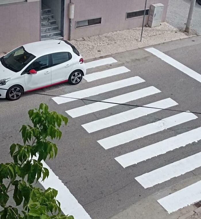 Poorly done job showing a car parked on a poorly painted and misaligned pedestrian crosswalk on the street.