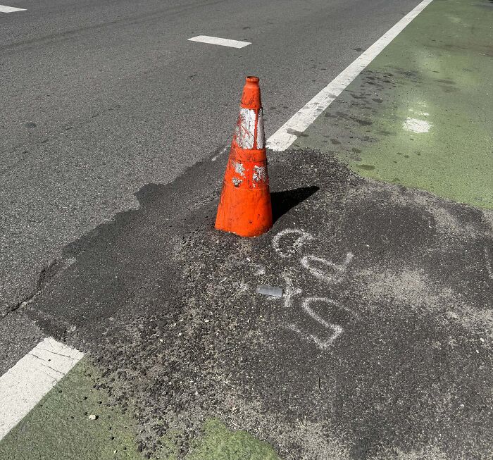 A traffic cone placed in the middle of uneven pavement patch showing poor job performance on road repair.