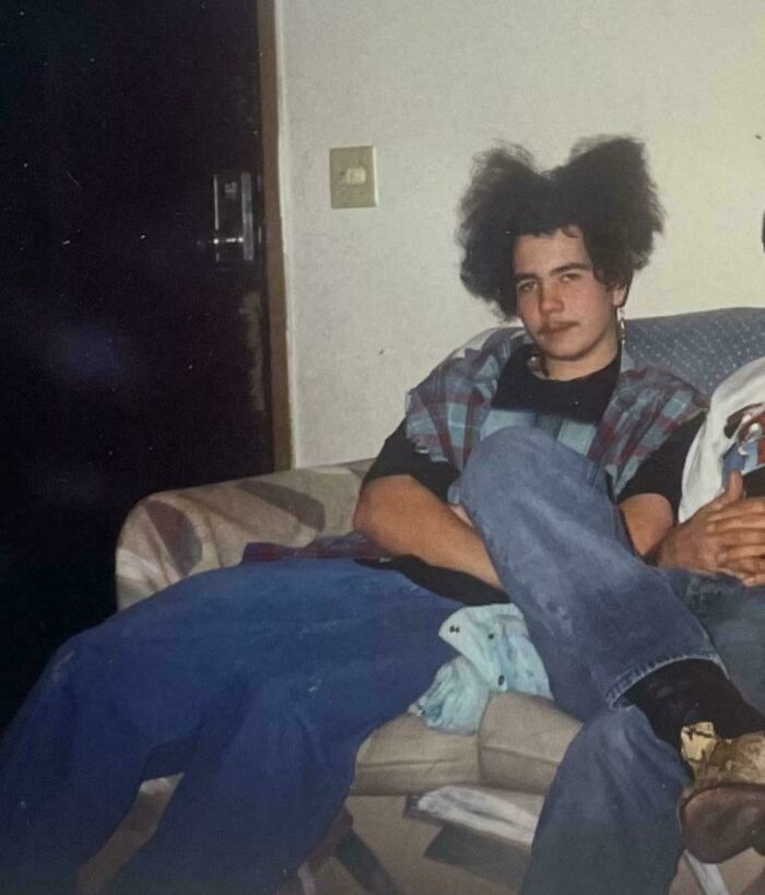 Teen boy with exaggerated fluffy hairstyle sitting on a couch, a classic awkward childhood photo moment.