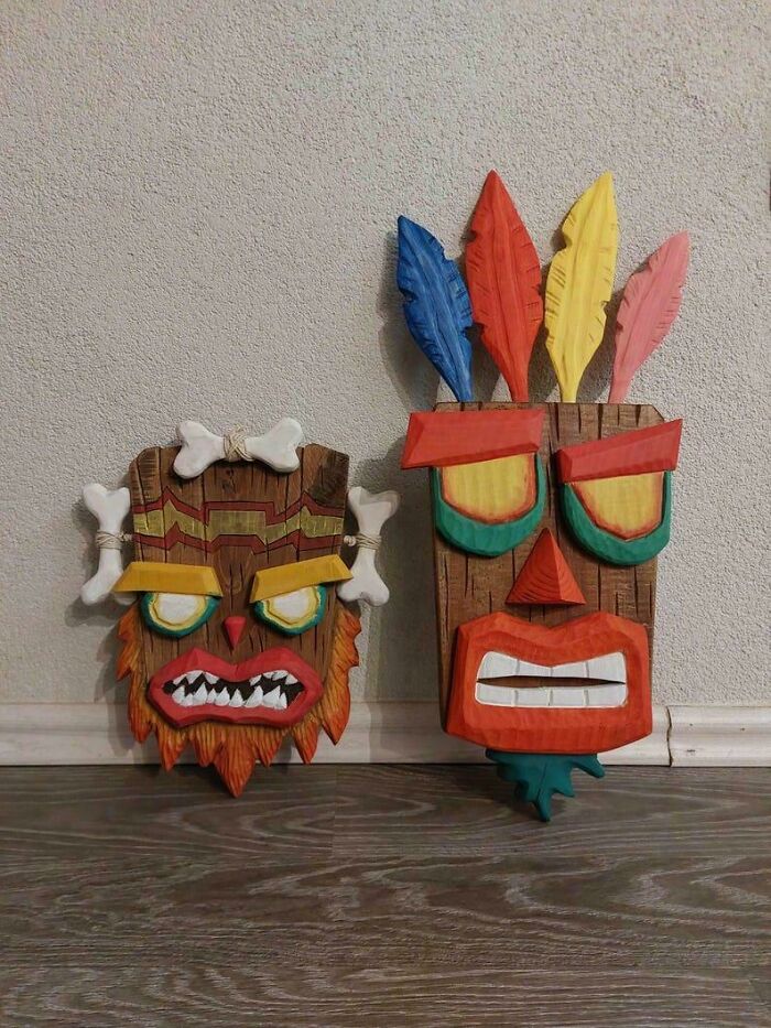 Two colorful carved wooden masks with bold facial features and feathers, showcasing impressive woodworking projects.