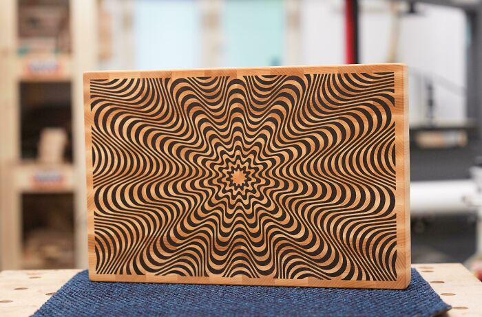 Woodworkers crafted an intricate optical illusion pattern on a polished wooden board displayed on a workbench.