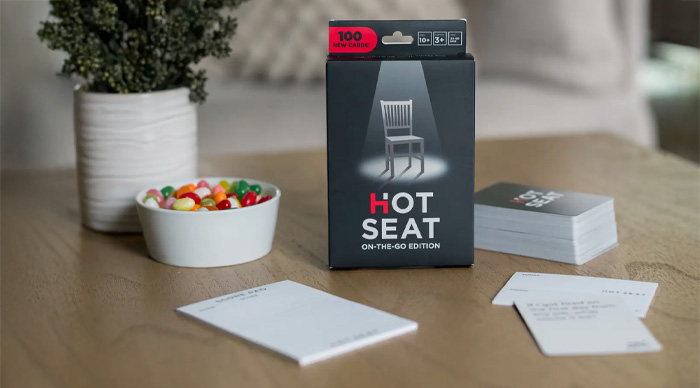 Party game Hot Seat box and cards arranged on a wooden table with a bowl of colorful jelly beans nearby
