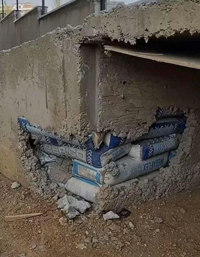 Concrete wall built over cement bags left exposed underneath, showing a poor and almost impressive job e*******n.