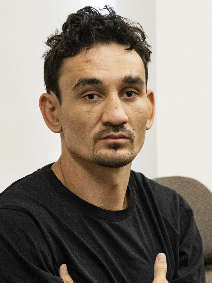Max Holloway in a black shirt sitting with arms crossed, showing a focused expression in an indoor setting.