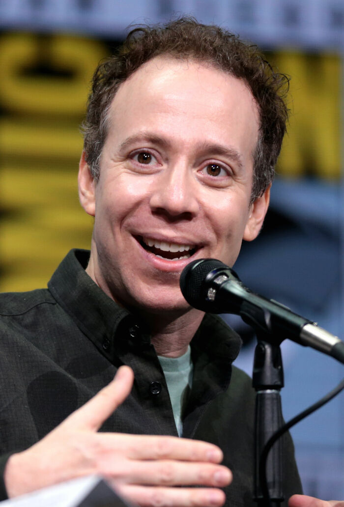 Kevin Sussman speaking into a microphone, smiling and gesturing during a public event or panel discussion.