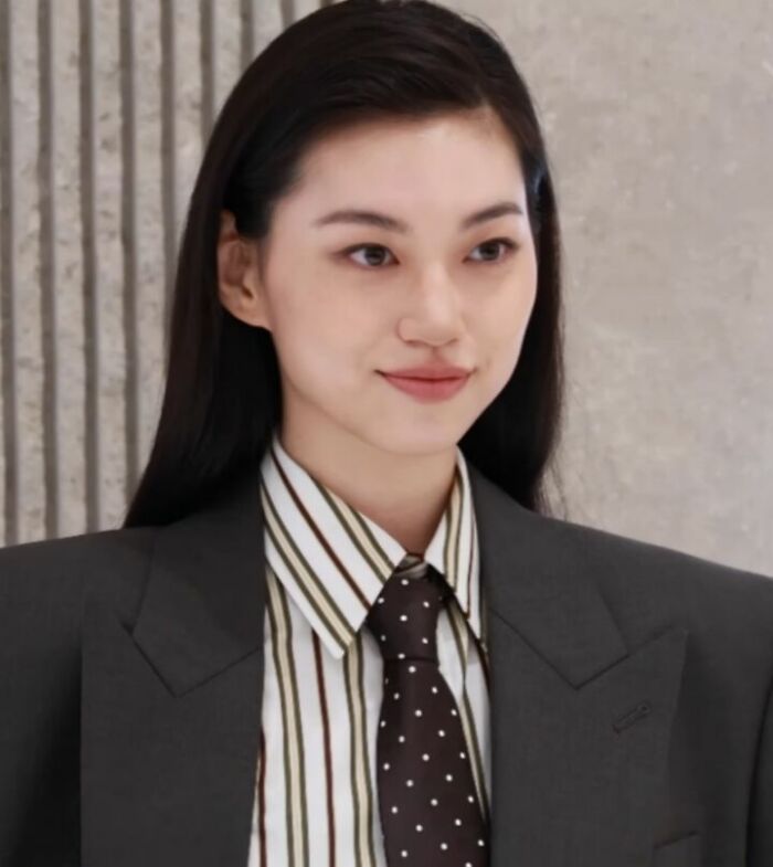 Kim Do-yeon wearing a striped shirt and dark suit jacket, smiling softly against a textured wall background