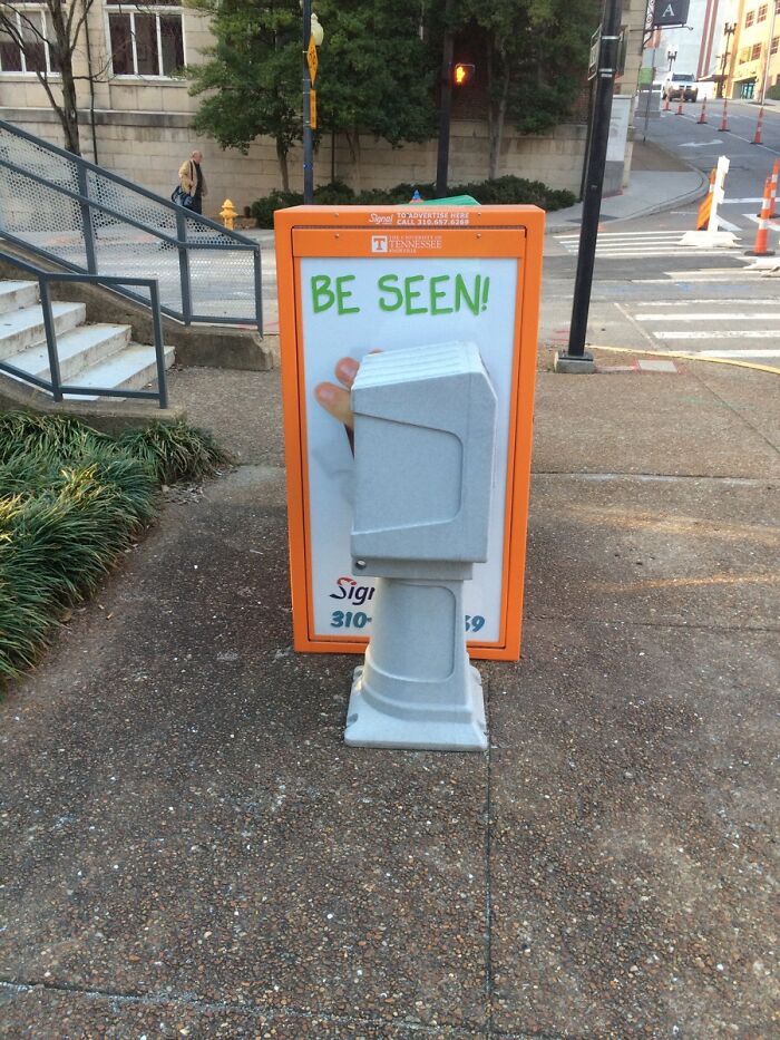 Gray utility box blocking a sidewalk sign on an urban street, an example of pointless things serving no purpose except for being funny.