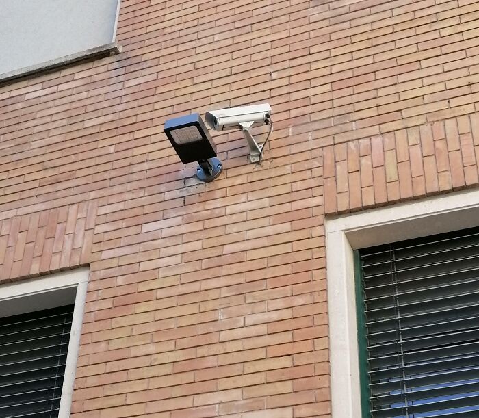 Security camera and light installed too close on brick wall, showing poor job e*******n and careless placement.