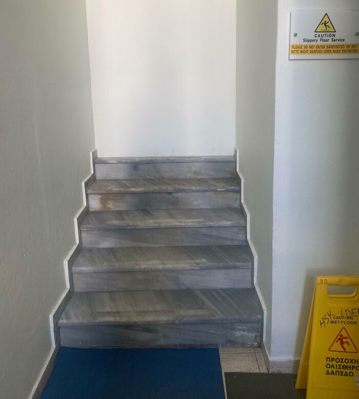 Stairs in a narrow hallway with slippery floor signs, showcasing a poorly executed job in safety placement.