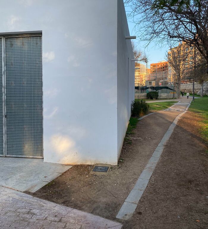Sidewalk abruptly ending at a white building with a narrow dirt path continuing, showing poor job e*******n in construction.