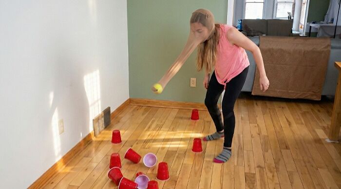Person playing a fun party game indoors with red plastic cups scattered on a wooden floor in a living room setting.