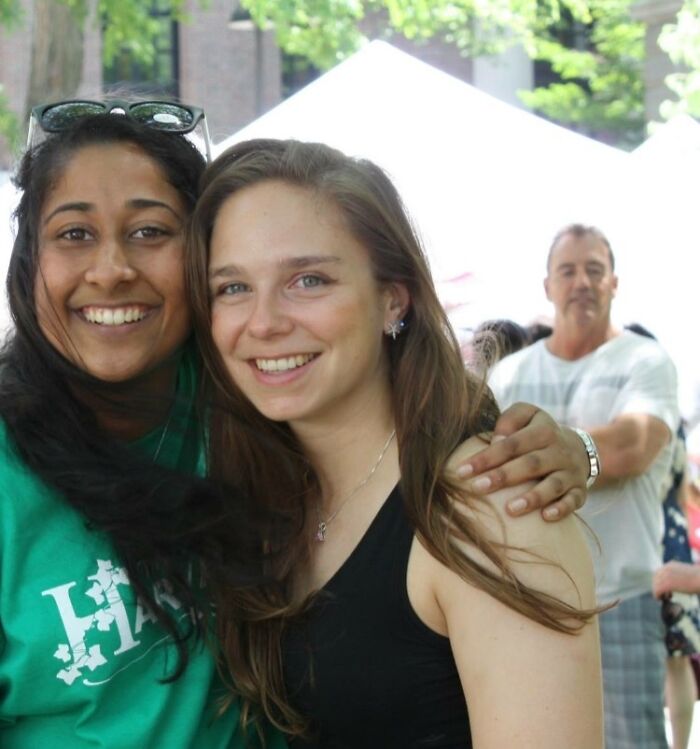 Two women smiling outdoors with a man in the background in a photo that is visually confusing your brain to catch up.
