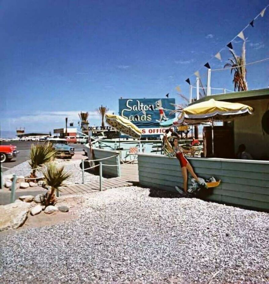 Vintage scene at Salton Sands with colorful umbrellas and a person in red swimsuit, a random picture worth going down a rabbit hole for.