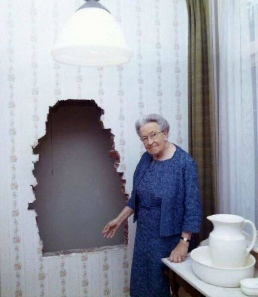 Elderly woman stands next to a large hole in a wall, an intriguing random picture worth going down a rabbit hole for