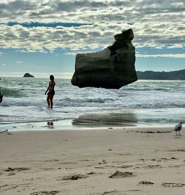 Person standing near ocean with large rock appearing to float, one of the photos so confusing your brain might need a moment to catch up