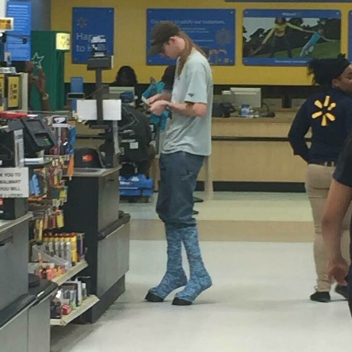 Customer wearing unusual footwear resembling blue leg warmers standing at a checkout in a Walmart store aisle.