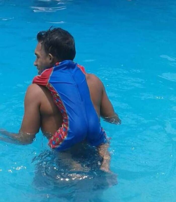 Man in a pool with a child wearing a blue and red swimsuit, creating a confusing visual effect for the brain to catch up.