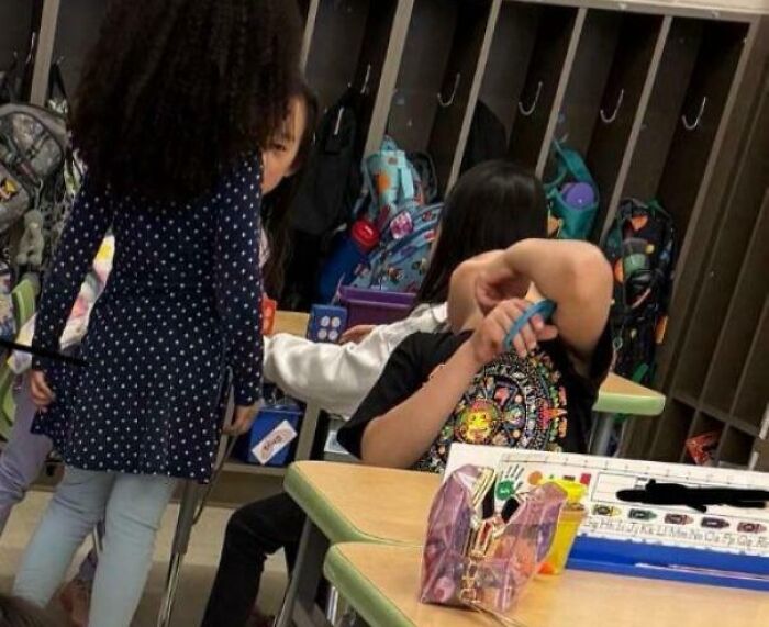 Children in a classroom with a confusing perspective where one child’s face seems hidden behind another’s arm, creating a brain-teasing photo.