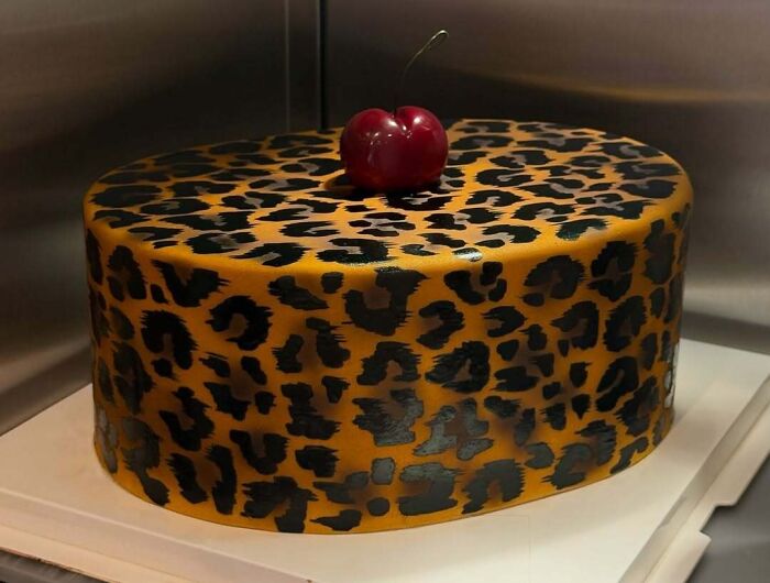 Round cake with a masterfully crafted leopard print design topped with a single cherry showcasing creativity in cake art.