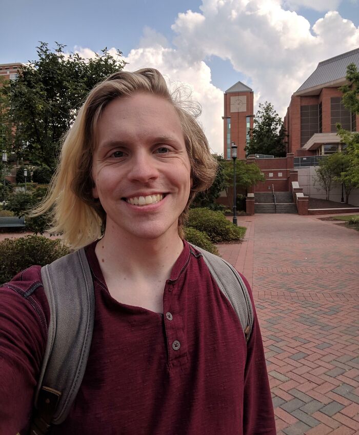 Young man smiling outdoors on a college campus, representing people who took a leap of faith making life decisions.