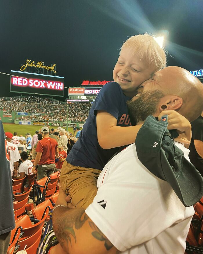 Heartwarming photo of a father hugging his smiling son at a baseball game celebrating a Red Sox win.