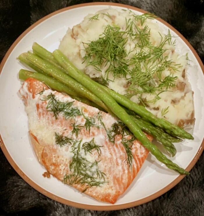 Salmon with fresh dill, steamed asparagus, and mashed potatoes served on a white plate, showcasing healthy meal choices.