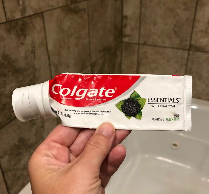 Hand holding a used Colgate toothpaste tube in a bathroom, illustrating a leap of faith in everyday choices.