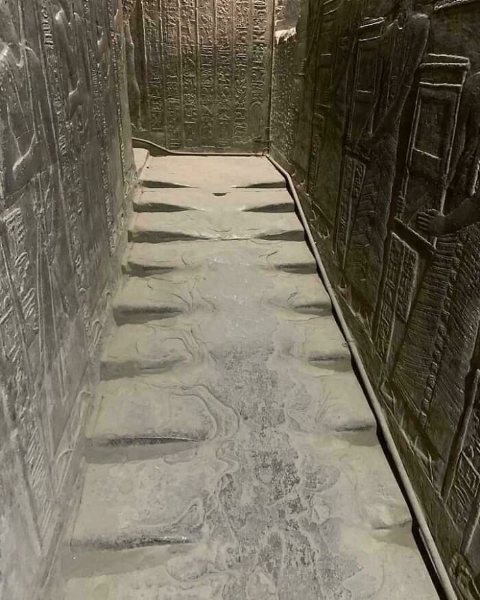 Ancient Egypt stone floor with carved grooves surrounded by hieroglyphs and wall reliefs inside historic tomb.