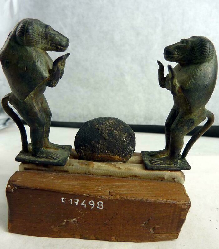 Ancient Egypt artifact showing two monkey statues standing on a wooden base holding a stone disc between them.