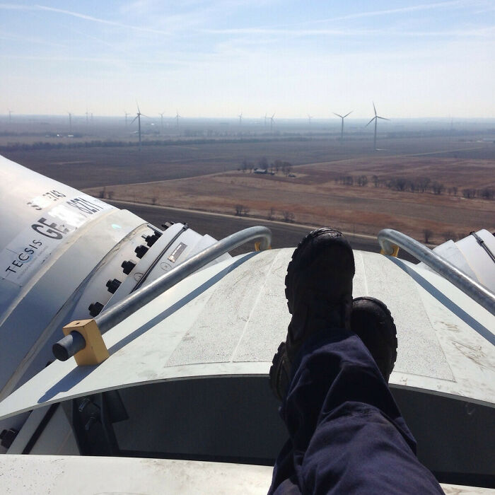 Technician resting on top of a wind turbine with a view of windmills and countryside, showcasing different jobs.