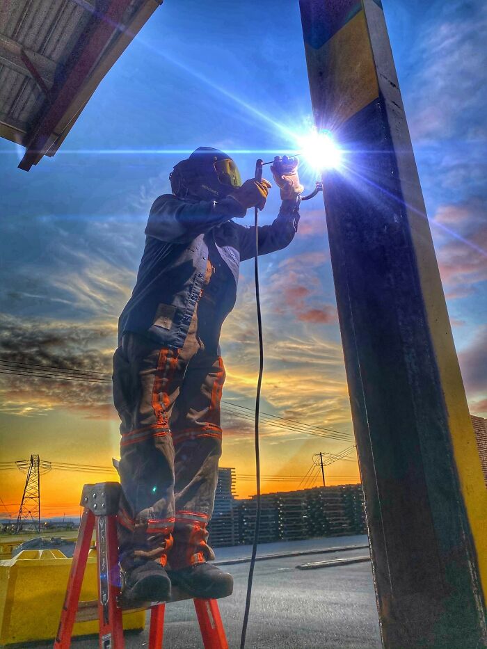 Welder working on a metal beam during sunset, showcasing different jobs that make a 9-to-5 more bearable.