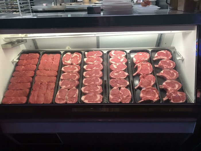 Butcher displaying fresh cuts of meat in a refrigerated case, highlighting different jobs that make a 9-to-5 more bearable.