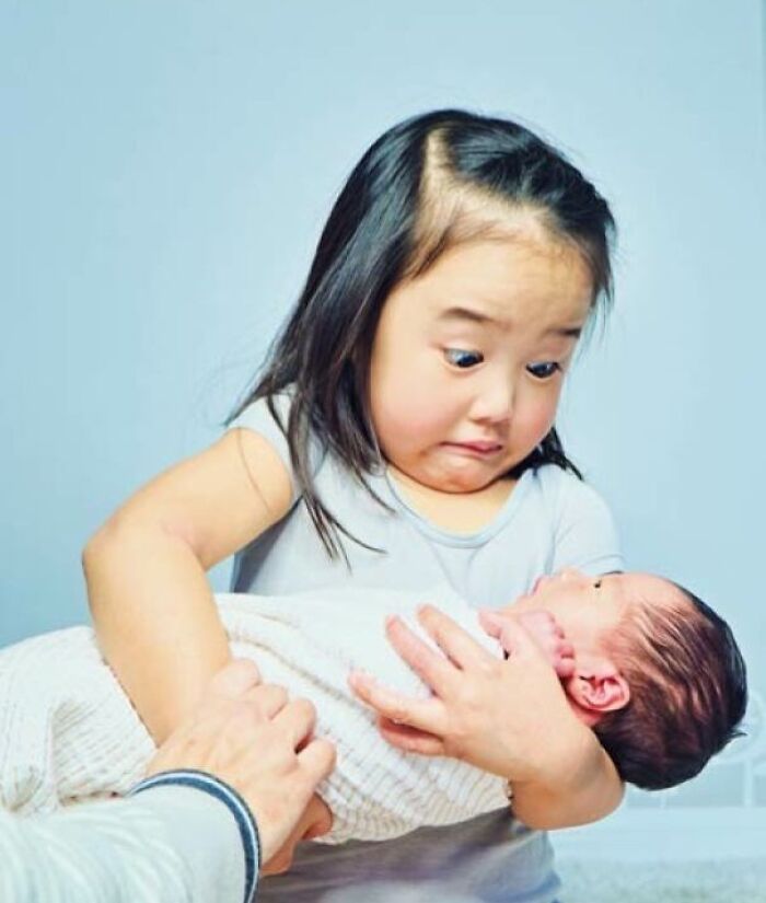 Young girl holding a baby with a surprised expression, one of the heartwarming photos that brighten your day.