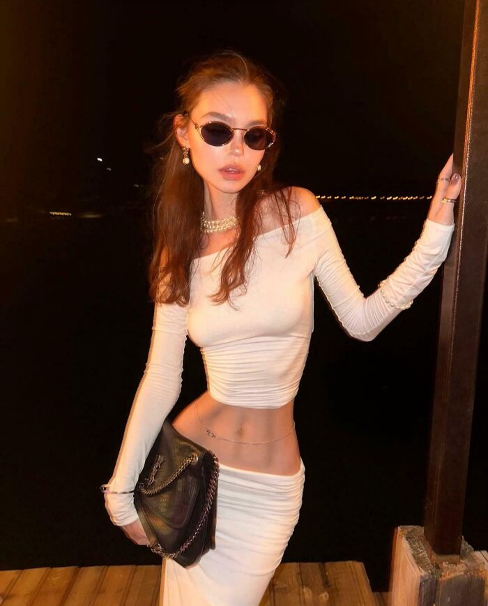 Young woman in stylish white outfit and sunglasses posing at night showing Instagram vs reality moments behind glam.